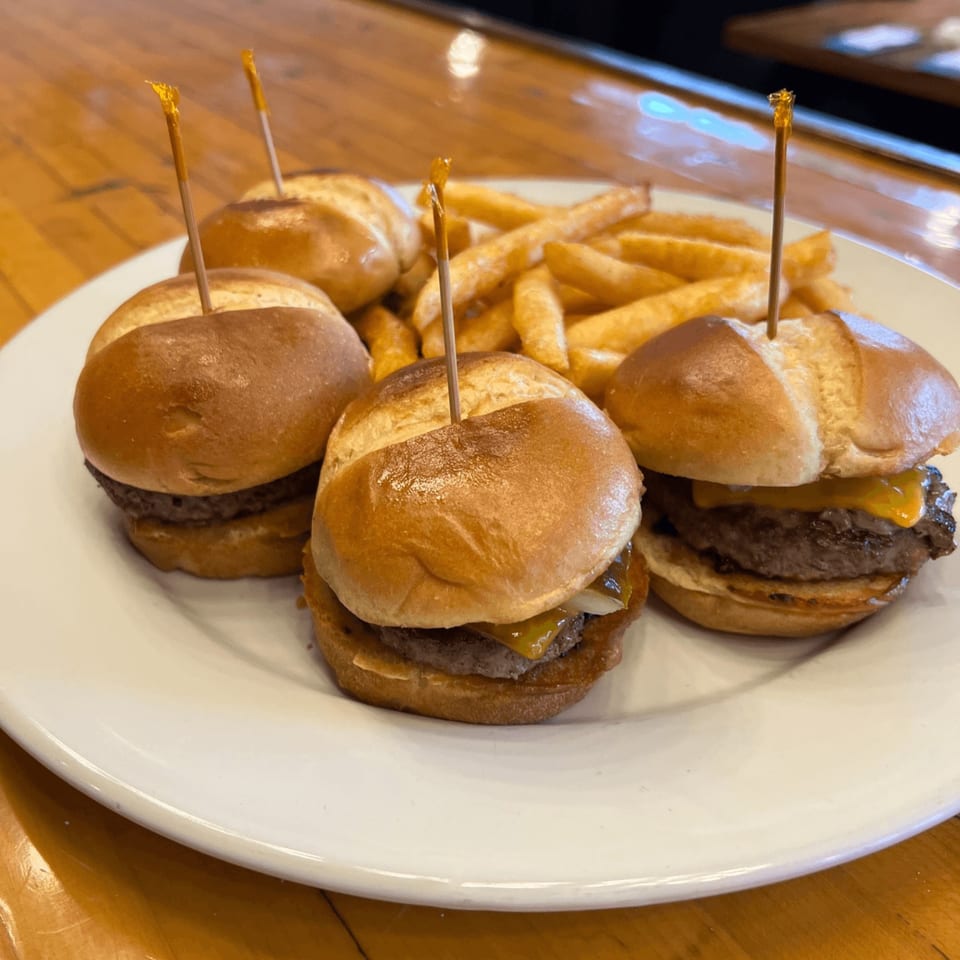 Four mini cheeseburger sliders with toothpicks and a side of golden french fries on a white plate.