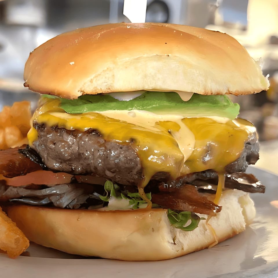 Acme Cafe's juicy burger with melted cheese, avocado, bacon, and fries on a white plate.