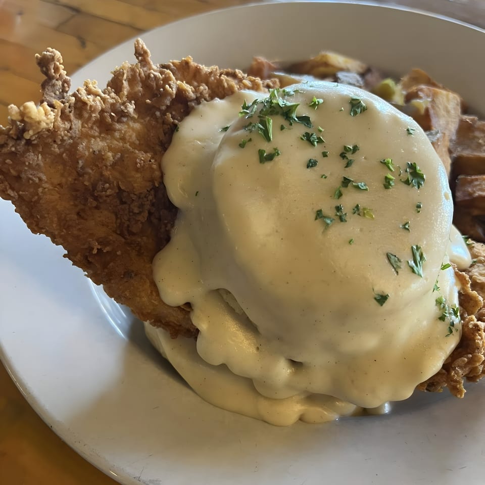 Acme Cafe's chicken fried steak with creamy gravy and parsley, served with roasted potatoes.
