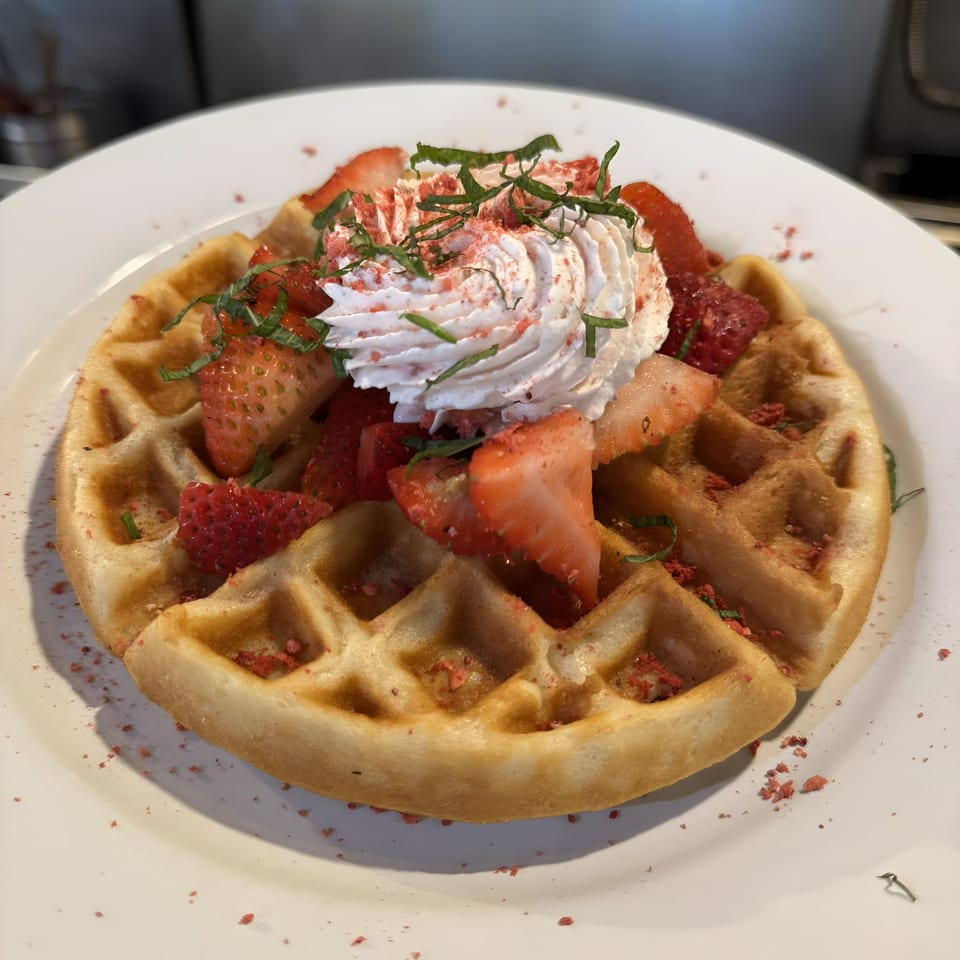 Golden waffle topped with fresh strawberries, whipped cream, and mint on a white plate.