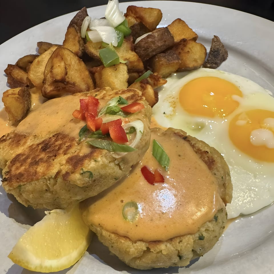 Acme Cafe's crab cakes with sauce, fried eggs, home fries, and a lemon wedge.