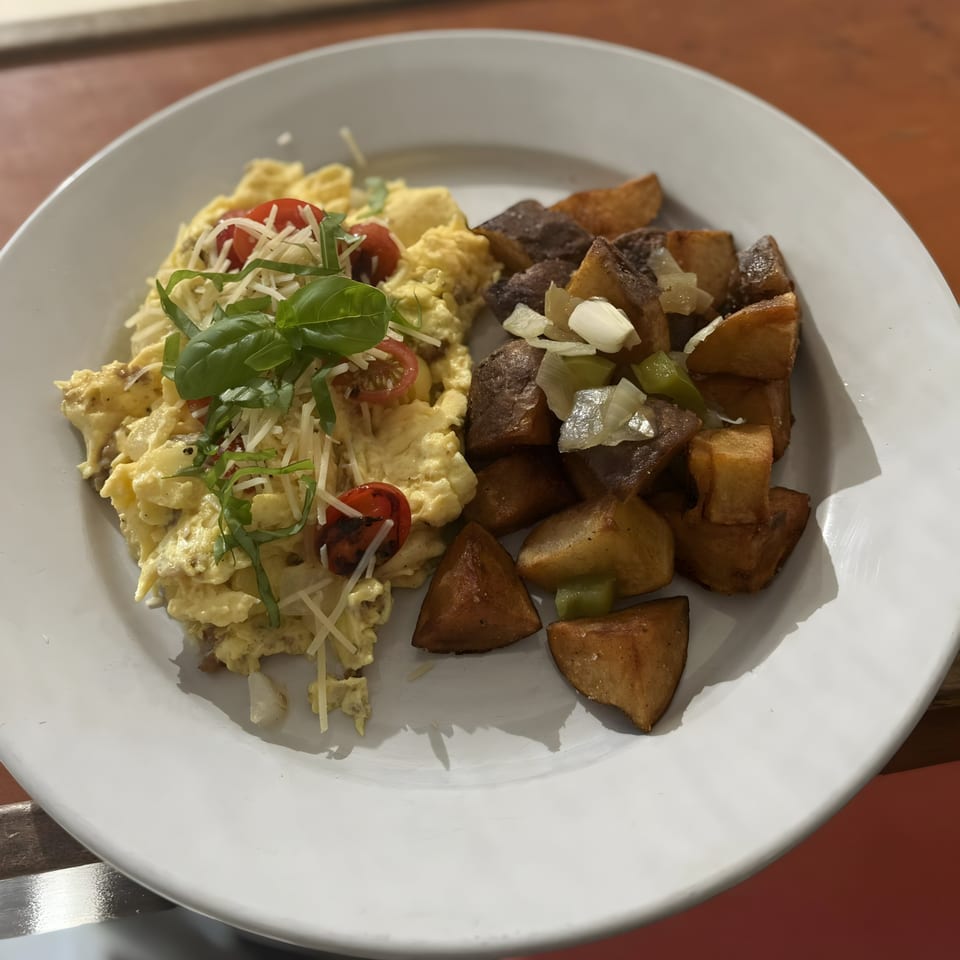 Scrambled eggs with cherry tomatoes, cheese, and basil, served with roasted potatoes and onions.