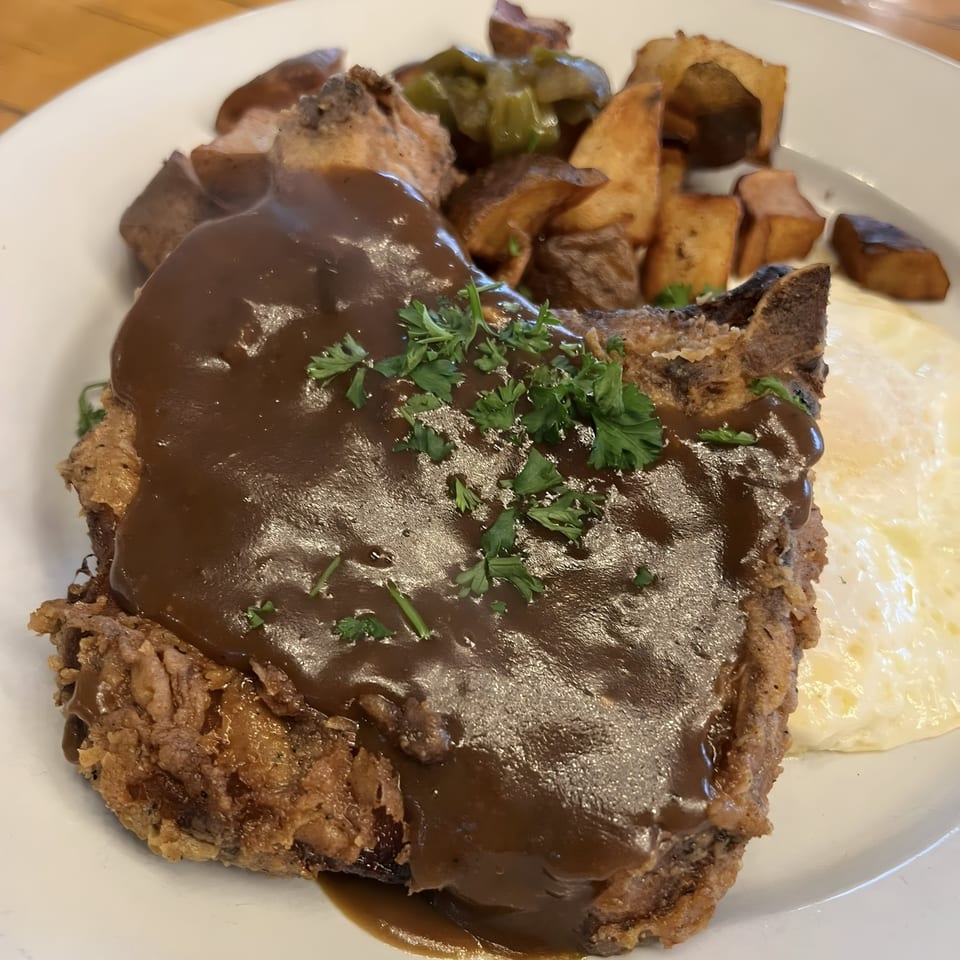 Chicken fried steak with gravy, home fries, and a fried egg on a white plate at Acme Cafe.